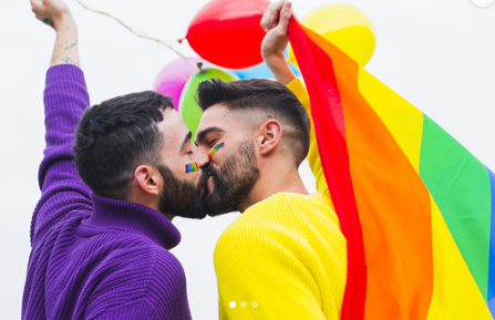 Casal se beijando com bandeira do arco-íris ao fundo